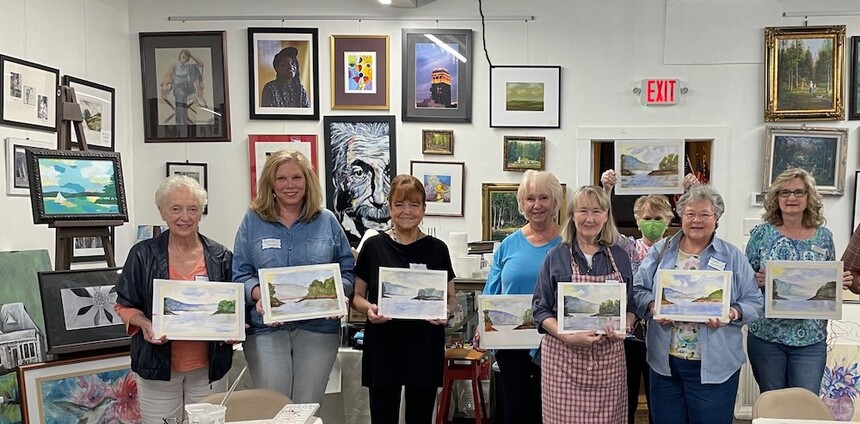 Art Class Participants pose with their paintings at art gallery with picture hanging system