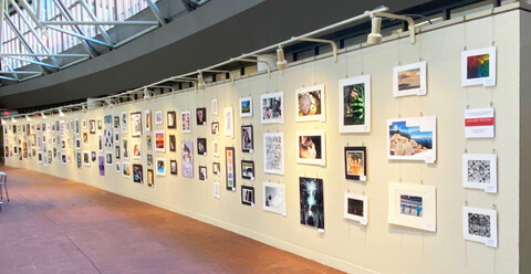 Panoramic view of student art being shown in public gallery space on art hanging system