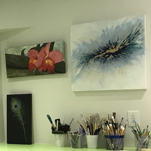 Artworks hung on picture hanging system in an art studio over table with brushes and pencils